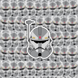May include: A gray and white clone trooper helmet sticker with a red triangle and a black antenna. The helmet has a white visor and a black stripe across the front. The sticker is surrounded by a white border.
