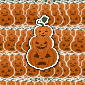 May include: A stack of three orange jack-o'-lantern stickers with different facial expressions. The stickers are arranged in a pyramid shape, with the smallest jack-o'-lantern on top and the largest on the bottom.