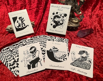 May include: A black and white tarot deck with the title "Bearded Journey Tarot" and the name "Doug Hammett". The cards feature black and white illustrations of people with beards and other imagery.