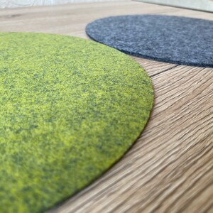 Op de afbeelding: Twee ronde vilt onderzetters, een groene en een grijze, op een houten oppervlak.