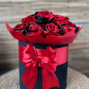 Peut inclure: Une boîte en velours noir avec un nœud en satin rouge, remplie d'un bouquet de roses en soie rouge et noire.
