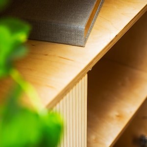 May include: Close-up of a light wood cabinet with open shelves. The cabinet has a textured wood grain and a light wood finish. The shelves are empty.