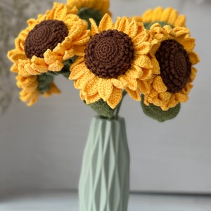 May include: A bouquet of crocheted sunflowers in a light green vase. The sunflowers are yellow with brown centers and green leaves.