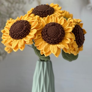 May include: A bouquet of crocheted sunflowers in a light green vase. The sunflowers are yellow with brown centers and green leaves.