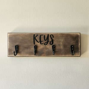 Peut inclure: Un porte-clés en bois avec trois crochets et le mot "KEYS" écrit en lettres noires.