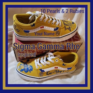 May include: A pair of yellow custom Vans sneakers with a blue and white design. The sneakers have the text "Ee-Yip!" and "Your Name" written on them. The sneakers are decorated with pearls and rubies. The sneakers are inspired by Sigma Gamma Rho.