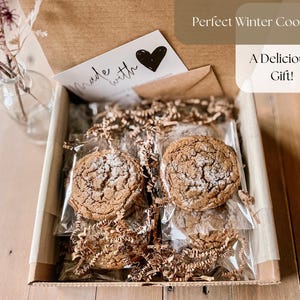 May include: A gift box with several cookies, packaged in clear plastic, and nestled in brown paper shreds. The box contains a card that says "Made with" and a black heart. The text "Perfect Winter Cookie" and "A Delicious Gift!" are also visible.