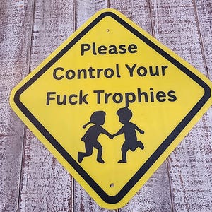 Könnte beinhalten: Ein rautenförmiges gelbes Metallschild mit schwarzem Rand und schwarzer Aufschrift "Please Control Your Fuck Trophies". Unter dem Text befindet sich eine schwarze Silhouette von zwei Kindern, die Händchen halten und zusammen rennen.