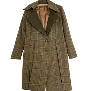 Op de afbeelding: Een lange vintage jas met een ruitpatroon in bruin-, groen- en goudtinten. De jas heeft een contrasterende olijfgroene kraag en een geplooide voorkant. Het heeft twee knopen en een beige voering.