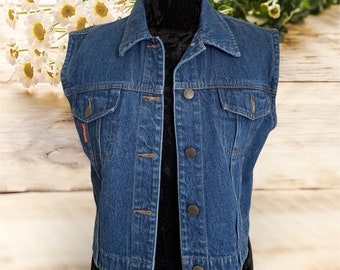Op de afbeelding: Een blauwe denimvest met een knoopsluiting en twee zakken. De vest is mouwloos en heeft een klassieke denimlook.