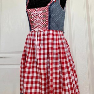 May include: A red and white gingham dirndl dress with a blue denim bodice and white lace trim. The bodice has a white ribbon lacing and silver buttons.