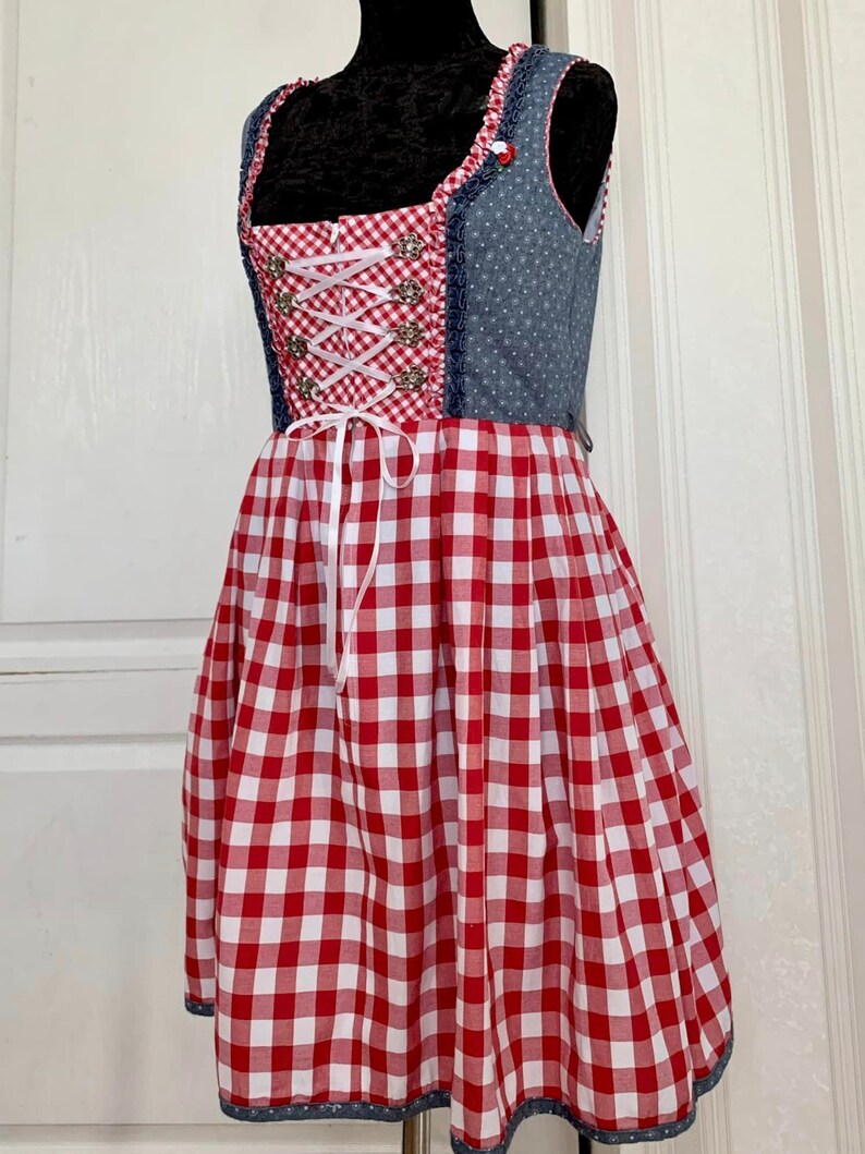 May include: A red and white gingham dirndl dress with a blue denim bodice and white lace trim. The bodice has a white ribbon lacing and silver buttons.