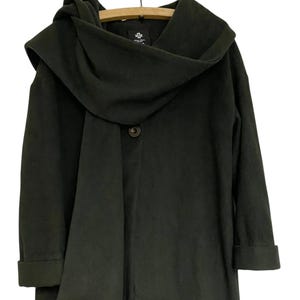 May include: Dark olive green hooded coat with a draped neckline and a single button fastening. The coat has long sleeves with folded cuffs and is hanging on a wooden hanger.