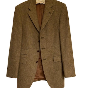 May include: A brown tweed blazer with a three-button closure and two front pockets. The blazer has a notched lapel and a brown interior lining. The fabric has a subtle herringbone pattern.