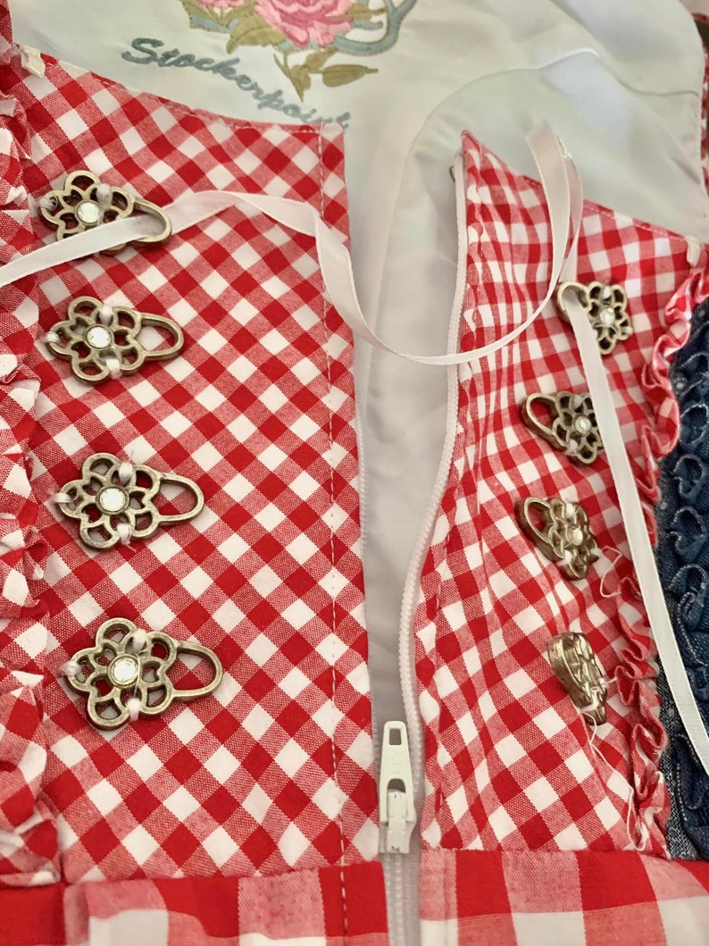 May include: Red and white gingham fabric with a zipper closure and decorative metal buttons. The fabric has a white ribbon tied around it.