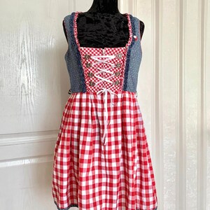 May include: A red and white gingham dirndl dress with a blue denim bodice and white lace trim. The bodice has a white ribbon lacing and silver buttons.