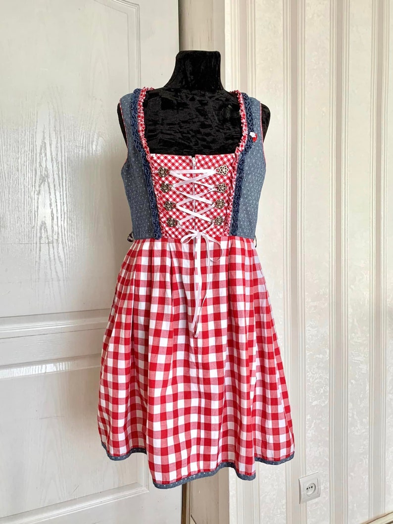 May include: A red and white gingham dirndl dress with a blue denim bodice and white lace trim. The bodice has a white ribbon lacing and silver buttons.