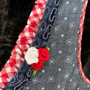 May include: A close-up of a blue denim fabric with white polka dots. The fabric has a red and white gingham trim and a white and red flower embellishment.