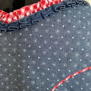 May include: A blue denim top with a white polka dot pattern and a red and white gingham trim. The trim is ruffled and sewn around the neckline.