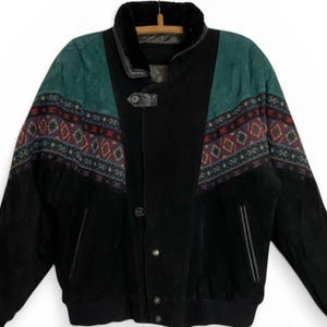 May include: Black suede jacket with a green yoke and patterned accents. The jacket features a button closure, a fur-lined collar, and a geometric design in shades of purple, red, and blue. The jacket has a classic bomber style.