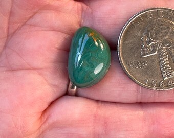 Può includere: Un cabochon di turchese verde con macchie dorate, incastonato in un anello d'argento. La pietra è circa delle dimensioni di una moneta da 25 centesimi di dollaro americano.
