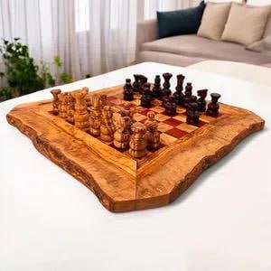 Op de afbeelding: Een houten schaakset met een rand met levende rand. Het bord heeft een rood-bruin geblokt patroon. De schaakstukken zijn bruin en bruin. De set wordt gepresenteerd op een wit oppervlak.