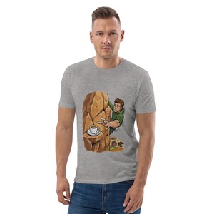 Könnte beinhalten: Graues T-Shirt mit einer Cartoon-Illustration einer Person, die eine Felswand erklimmt. Der Felsen hat eine Kaffeetasse auf einem Vorsprung. Der Kletterer greift nach dem Felsen. Das Shirt ist aus weichem Material.