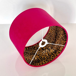 Può includere: Un paralume rosa con una fodera a stampa leopardata. Il paralume è in tessuto e ha un anello di metallo bianco in cima.