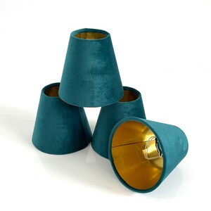 May include: Four teal blue velvet lampshades with gold lining. The lampshades are stacked on top of each other.