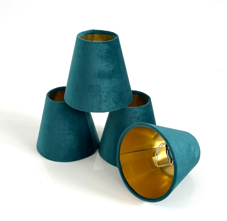 May include: Four teal blue velvet lampshades with gold lining. The lampshades are stacked on top of each other.
