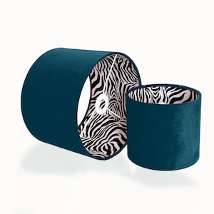 Può includere: Due paralumi in velluto blu petrolio con fodera a stampa zebrata. Il paralume più grande è sdraiato di lato, mentre quello più piccolo è in piedi.