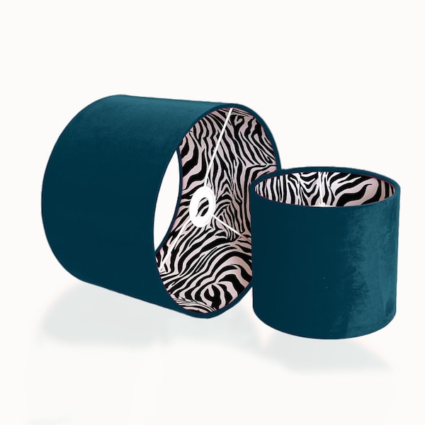 Könnte beinhalten: Zwei Lampenschirme aus tealblauem Samt mit einer Zebra-Muster-Futter. Der größere Lampenschirm liegt auf der Seite, während der kleinere Lampenschirm aufrecht steht.