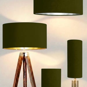 Könnte beinhalten: Eine Auswahl an olivgrünen Lampenschirmen in verschiedenen Größen und Formen. Das Bild zeigt eine Hängeleuchte, eine Stehlampe mit Holzstativ und zwei Tischlampen. Die zylindrischen Lampenschirme haben eine strukturierte Oberfläche. Die Lampenschirme sind dunkelgrün.