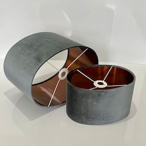 May include: Two gray oval lampshades with a copper lining. The larger lampshade is in the background and the smaller lampshade is in the foreground.