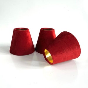 May include: Three red velvet lampshades with gold trim. The lampshades are cone-shaped and have a smooth, soft texture.