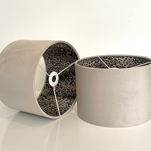 Può includere: Due paralumi in velluto grigio con fodera a stampa leopardata. I paralumi sono cilindrici e hanno un cordoncino bianco.