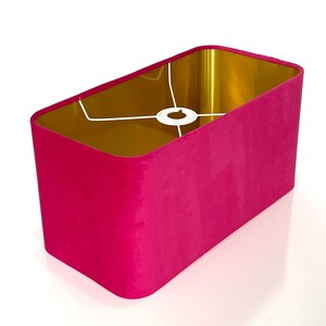 Può includere: Un paralume rettangolare con un esterno in velluto rosa e un interno dorato. Il paralume ha una struttura in metallo bianco per la lampadina.