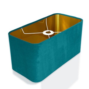 May include: Teal blue rectangular lampshade with a gold interior. The shade has a white cord and a white metal frame.