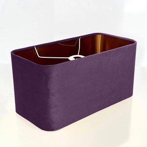 Può includere: Un paralume rettangolare in velluto viola scuro. Il paralume ha un interno bianco e una struttura in metallo bianco.