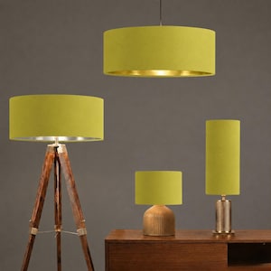 May include: A collection of lime green lampshades in various shapes and sizes. The lampshades are cylindrical and have a soft, textured appearance. One lampshade hangs from the ceiling, while others sit on wooden and metal lamp bases.