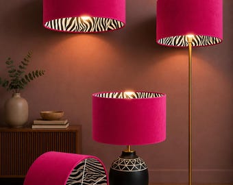 May include: A collection of magenta lampshades with a zebra print interior. The lampshades are cylindrical and come in various styles, including pendant, table, and floor lamps. The lamps are set against a dark brown wall.