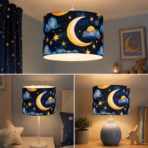 May include: A celestial-themed lampshade with a navy blue background, featuring a crescent moon, stars, and clouds. The lampshade is cylindrical and is shown hanging from the ceiling and on two different lamp bases. The lampshade is a decorative element for a child's room.