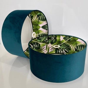 Peut inclure: Deux abat-jours en velours bleu sarcelle avec une doublure à imprimé de feuilles tropicales. Les abat-jours sont empilés l'un sur l'autre.