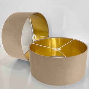 Op de afbeelding: Twee beige lampenkappen met gouden binnenkant. De lampenkappen zijn gemaakt van een zachte, fluweelachtige stof.