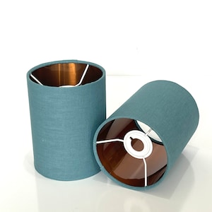 May include: Two teal blue lampshades with a copper lining. The lampshades are made of a textured fabric.