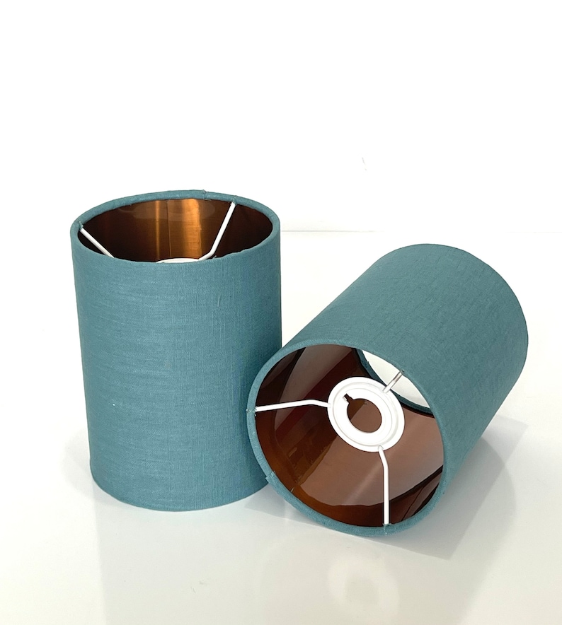 May include: Two teal blue lampshades with a copper lining. The lampshades are made of a textured fabric.
