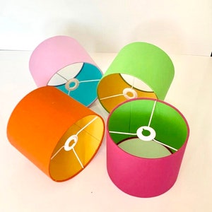 Puede incluir: Cuatro pantallas de lámpara con diferentes forros interiores y exteriores de colores. Las pantallas de lámpara son rosa, verde, naranja y rosa con forro verde.