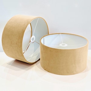 May include: Two beige lampshades with white interiors. The lampshades are made of a soft, textured fabric.
