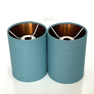 May include: Two teal blue lampshades with a copper lining. The lampshades are made of a textured fabric.