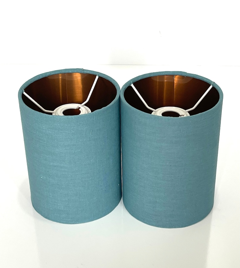 May include: Two teal blue lampshades with a copper lining. The lampshades are made of a textured fabric.